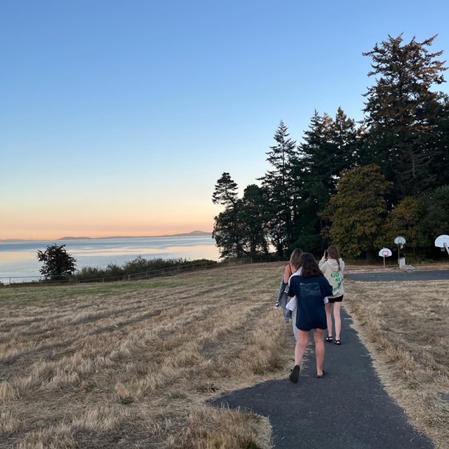 3 girls walking along the beach with orange and blue sun setting skies.