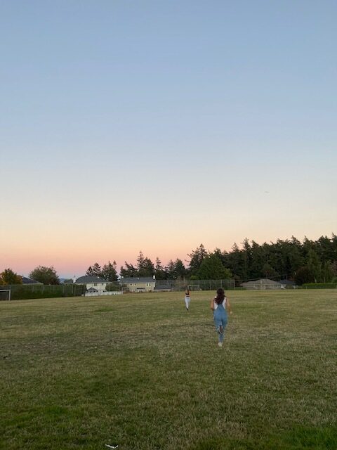 Two girls, Allie's roommates, running in a filed with a sunset behind them.