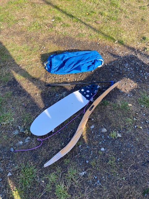 A sailboat rudderboard and tiller lying in the grass.